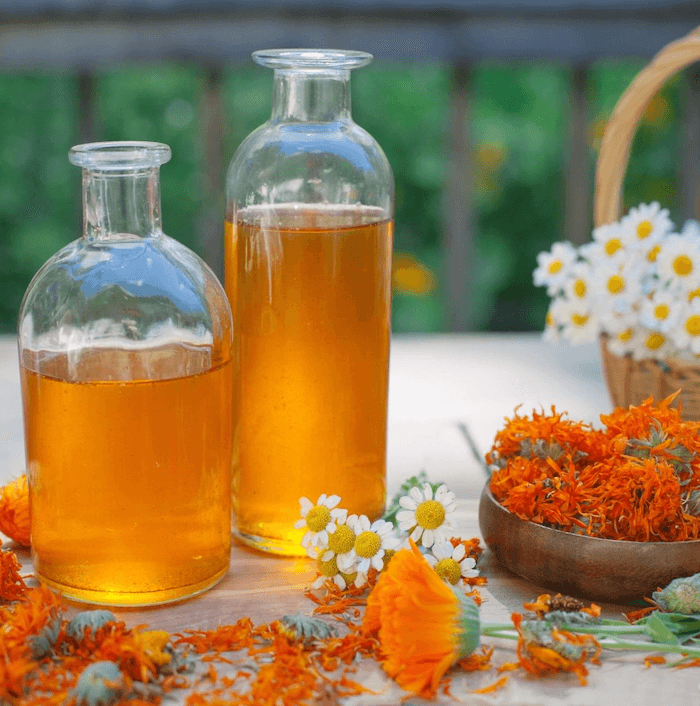 Glass jars of herbal oil on a table with dried calendula around